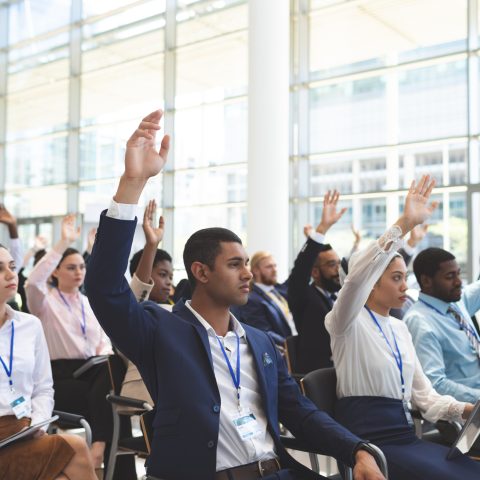 Front view of diverse business people raising hands in business seminar in office building