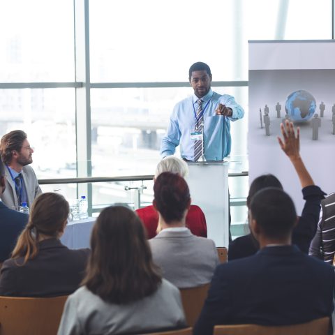 Rear view of mixed race businesswoman raising hand during business seminar in modern office building